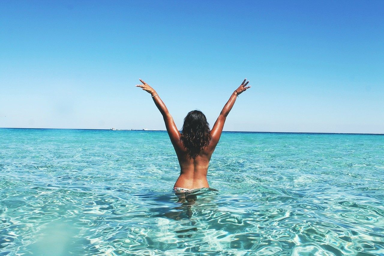Trabajar Australia chica morena de espaldas con los brazos levantados en el mar
